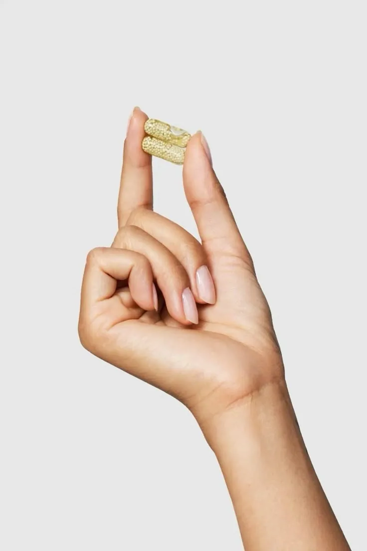 A hand holding two supplement capsules